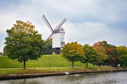 Traditional windmill called Bonne-Chièremolen on rampart Kruisvest in the historic town of Brugge, Belgium. Trees with autumn leaf color along the canal.