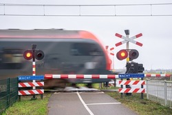 A train passes a railway crossing at high speed. Train is blurred by the speed of the train. Dutch text on the blue signs means: Wait until the red light is off, another train may come.