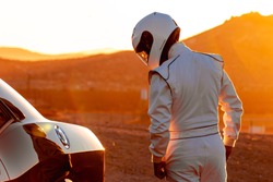 A Helmet Wearing Race Car Driver In The Early Morning Sun Looking At His Car Before Starting