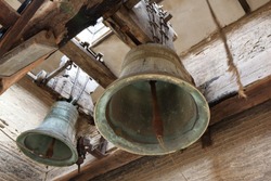 A close sight of two big ancient bells with their clappers and yokes, seen from below, in the belltower of Mary Magdalene church (Iglesia de la Madalena) in Tarazona, Aragon, Spain