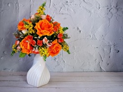Orange roses artificial flowers bouquet in vase on table, copy space for text or writing ,texture background or wallpaper ,mother's day ,still life ,women's day festive background ,colorful elegant 