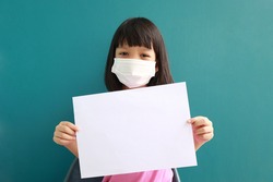 Thai girl with cute face Wear a white mask on the face to prevent toxic dust and the COVID-19 virus. Epidemic Her hand holding a white paper There is room to write a message. The background is green. 