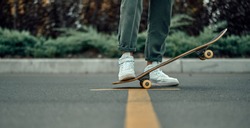 Cropped view of a stylish man in white sneakers and green pants with a skateboard, on a yellow crosswalk.