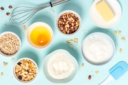 Ingredients for baking oat cookies with nuts and candied fruits on a blue background, top view, flat lay. Flour, butter, egg, oatmeal, sugar and nuts in bowls on the table