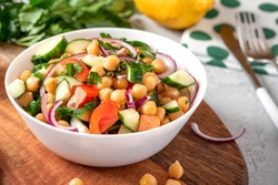 Chickpea salad with tomatoes, cucumber, parsley, onions, olive oil and lemon in a bowl on a served table. Tasty and healthy vegan food.