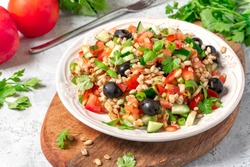 Pearl barley salad with vegetables in a plate close-up. Boiled pearl barley with tomatoes, cucumbers, olives, parsley and basil. Vegan and vegetarian food.