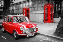 A classic red mini parked in front of two red phone boxes in London