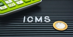 Brazilian economy and taxes. The initials ICMS for Tax on Circulation of Goods and Services written in Brazilian Portuguese. A calculator and 1 Real coin in the image composition.

