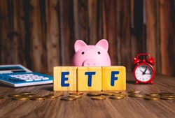 The initials ETF of the Exchange Traded Fund, in English, written on wooden cubes. A calculator, an alarm clock and some coins in the image composition.
