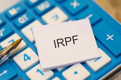 The initials IRPF refer to personal income tax on a piece of paper over a blue calculator. Brazilian economy and finance.
