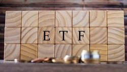 The initials ETF of Exchange Traded Fund inscribed on wooden cubes with a pile of coins in the composition. Economy and investments.
