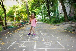 Little cute girl 4 y.o. playing hopscotch on playground outdoors. Lifestyle kid portrait outdoor.