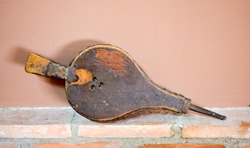close up of an old bellows made in leather and wood. The bellows is rested on a wall of bricks and an a brown background. Horizontal photo