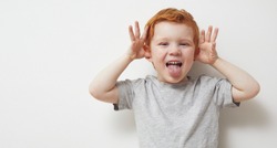 Portrait of a redhead ginger boy, child and toddler being silly and having fun in front of camera, showing a silly face and emotions.