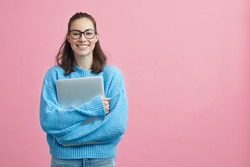 Cute looking girl, student, woman and female in studio holding her laptop or computer in arms beside copy space. Pink and blue colorful portrait on pink background. 