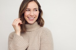 Portrait of young happy beautiful woman smiling and standing isolated on white background in a warm sweater. Young female girl with a perfect smile looking right.