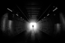 Dreaming, man in dark tunnel. Freedom light in tunnel. Silhouetted desaturated. Silhouette of a woman walking into the light. Light at the end of the tunnel. business man in silhouette walking