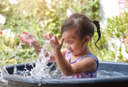 Asian child girl hit water while playing water in the basin. Happy girl in the garden.