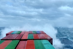 A container ship during stormy weather, water spraying on deck and containers