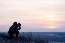 Pray. Prayer. Repentance. A man on his knees. Christian. Silhouette of a man on a blue sky background. Kneeling Prayer to God. Glorification.