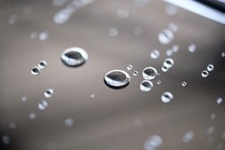 Water droplet on the car hood. Water beading after rain or car wash on black shiny paint surface. Beading created by ceramic coat or paint sealant with high surface tension. Water drop background.