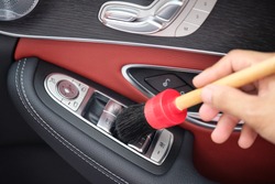 Auto detailer using detailing brush for cleaning dust in car window switch. Male hand cleaning car interior & upholstery with detail brush. Focus on brush. Car detailing concept. Car wash background.