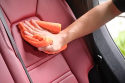 Man's hand cleaning red interior in luxury car with microfiber cloth. Hand wipe down leather seat of sports car.  Interior car detail and leather seat repair & cleaning background. Car wash concept.
