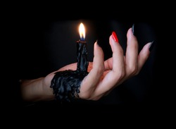 Black Candle melted on hand in black background. For halloween's concept. Felling darkness with light of flame burning from the supernatural.