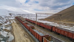 Railway station in mining industry. Freight train open wagons with ore. Train transportation on railway with mine stones at a snowy winter day in mountainous landscape. Full and empty containers