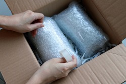 Woman’s hands packing fragile items with plastic air bubble wrapped and adhesive tape and putting in a brown cardboard parcel box.