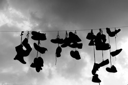Silhouette of tied shoes hanging on a wire. Shoe-tossing, also known as shoefiti, is the act of  throwing a pair of laced shoes onto raised wires