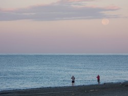 Lowlight photo of early morning fishing in the Mediterranean Sea. Two fishermen, calm sea, dawn sky and a full moon