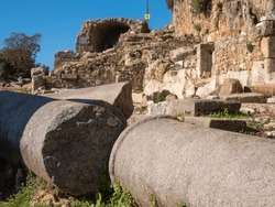 Fragments of a granite column against the backdrop of the ruins of the ancient city of Syedra, located on the slope of the Taurus Mountains, South Turkey, on a sunny day