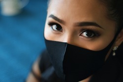 close up asian women wearing black protection face mask. bold eyes make up. blue background 