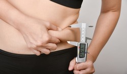 Fat woman measuring her belly fat by vernier caliper scale, Overweight woman check out her obesity, Woman muffin top waistline.