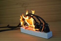 On fire multi socket with the connected power strip with a bunch of plugs on wood background
