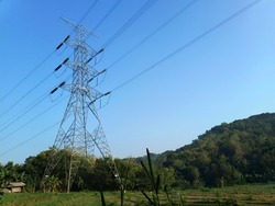 High-voltage electric tower poles that connect the islands of Java and Bali, with natural blue sky and mountainous background 