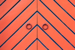 Orange double door and ring knockers. Diagonal black and blue stripes in fishbone pattern. Detail. In Tallinn, Estonia.