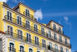 Traditional apartment building in Lisbon Portugal - exterior. Bright yellow and white facade with tall windows and long balconies. Portuguese style vintage house with multiple condos.