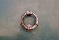 Close-up of a door knocker in the shape of an uroboros, an ancient symbol depicting a serpent (or dragon) eating its own tail, often interpreted as a symbol for eternal cyclic renewal, Italy