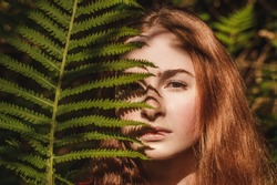 The young woman with fern leaf and shadow on face. Nature concept. Close up portrait.