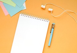 Stationery and headphones lie on a juicy orange background.