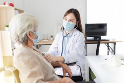 Asian doctor talk with old female patient about disease symptom, doctor use stethoscope listening lung of patient, elderly health check up , they wear surgical mask on white background, corona virus 
