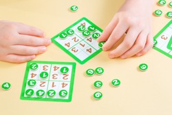 Hands of a child playing sudoku board game filling the card with number tokens. Education concept with copy space