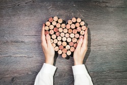 Two female hands holding a heart made of wine corks. Flat lay on wooden rustic background. 14 February. Passion, love and feelings St Valentine's Day Card celebration concept with copy space