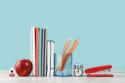 Organized office and school orange and pastel blue stationery, notebooks pencils scissors and alarm clock with red apple on grey wooden desk. Copy space for back to school education and craft concept