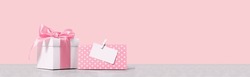 White gift box with shining pink ribbon bow on pink background with mockup gift card. Gift or holiday concept. Mothers Day, birthday wedding or St Valentines day banner with copy space