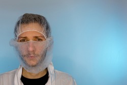 An adult male dressed in a white lab coat with a hair net and beard net on. Ready to work in a clean room or laboratory