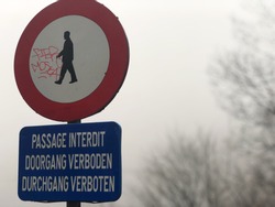 No entry sign with graffiti in three different languages, French, Dutch, German. And cloudy weather.