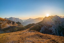 beautiful view over the Julian Alps with the sun setting over a beautiful mountain ridge on a sunny day in autumn. Enjoying beautiful mountain vistas with a sun star while traveling in Europe. 